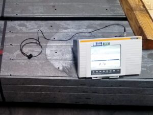 A stack of painted metal flat bars and an ultrasonic tester for measuring coating weight and thickness.