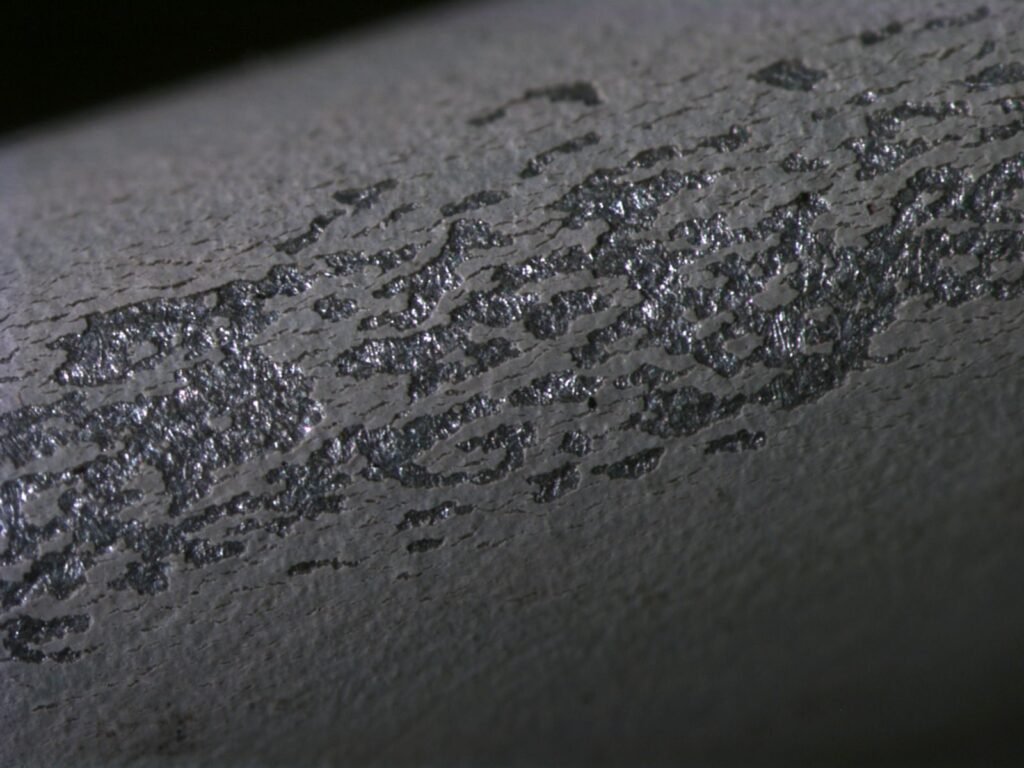 A coat of grey paint after an adhesion test. Flakes of coating have been ripped from the substrate.