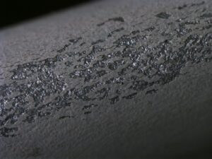 A coat of grey paint after an adhesion test. Flakes of coating have been ripped from the substrate.