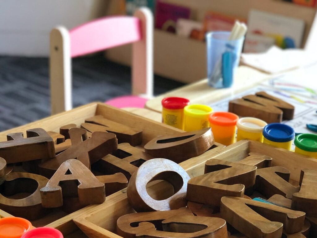 Educational toys for a preschool. A pile of wooden blocks shaped like letters. Multi-colored modeling clay containers.