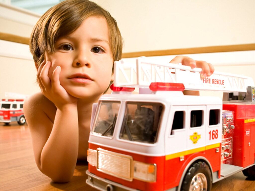 A small boy plays with a toy firetruck