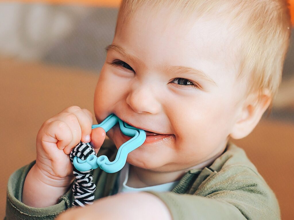 A baby sucks on a blue pacifier and grins