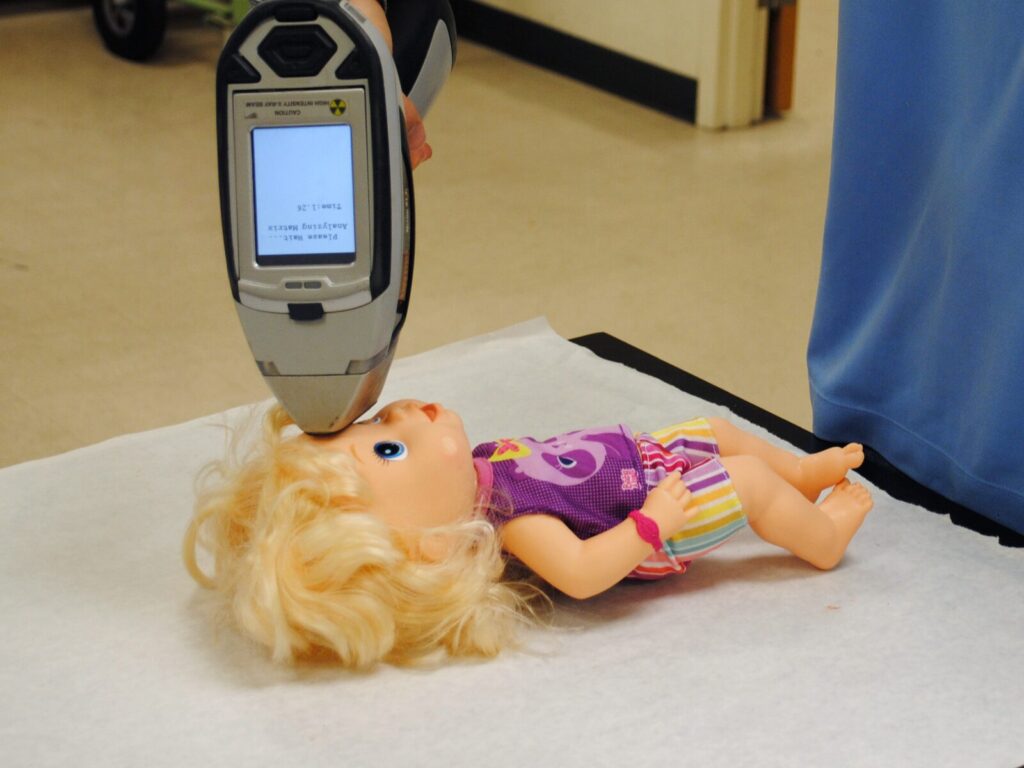 Chemist points an XRF tester at a toy doll for positive material identification.
