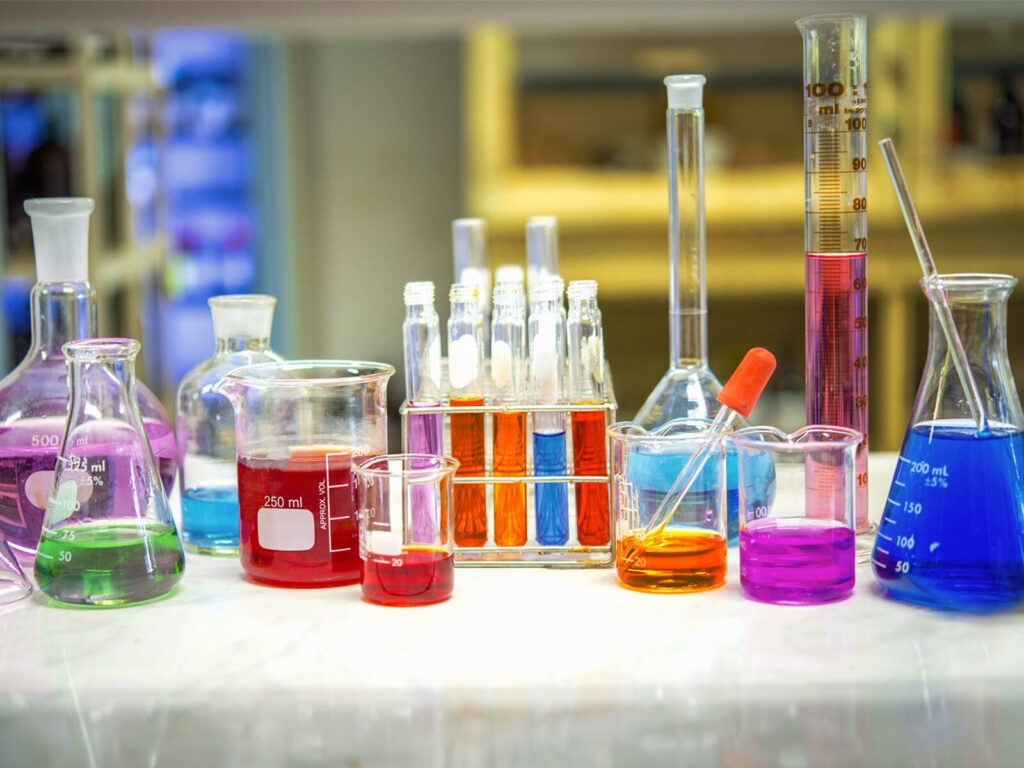 A tabletop of multicolored liquid samples in glass beakers and flasks.