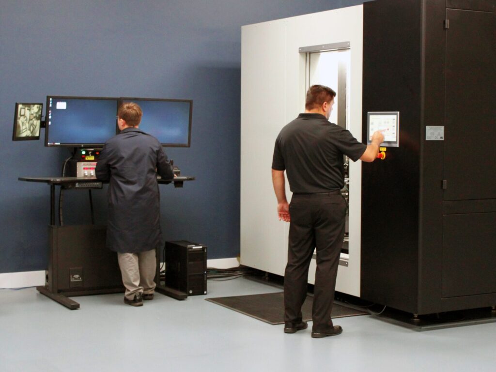 Two lab technicians operate a computed tomography machine and computer display of the 3D scan