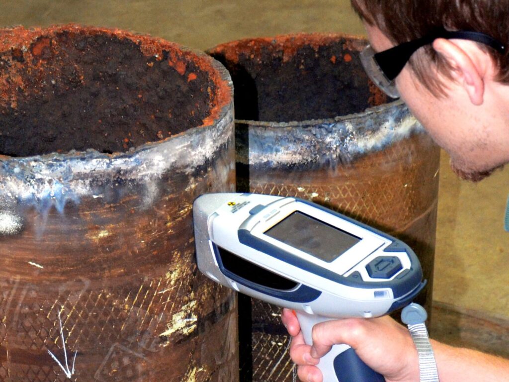 Technician uses a handheld X-ray fluorescent (XRF) spectrometer for positive material identification of a rusted metal pipe.