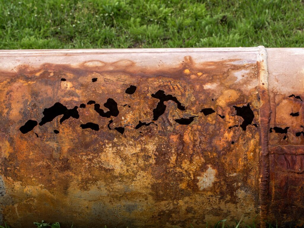 Corroded above ground pipe. The corrosion has formed holes in the pipe and caused thinning in other parts.