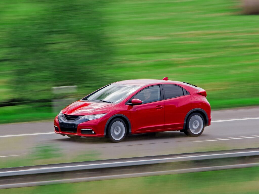 A red car in front of a blurry grass background