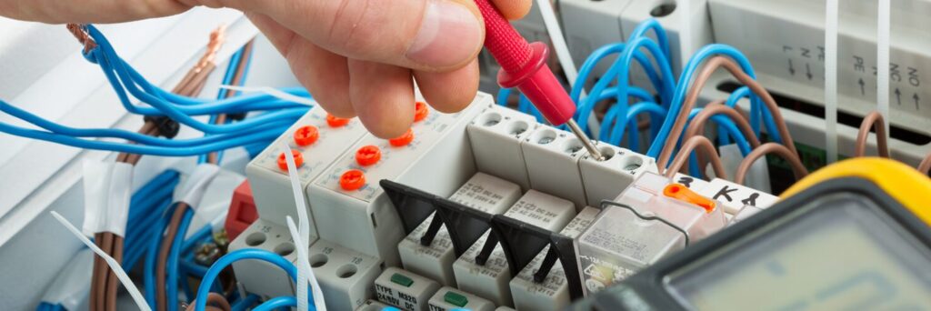 A technician uses a voltmeter probe on an electrical switchgear cabinet.
