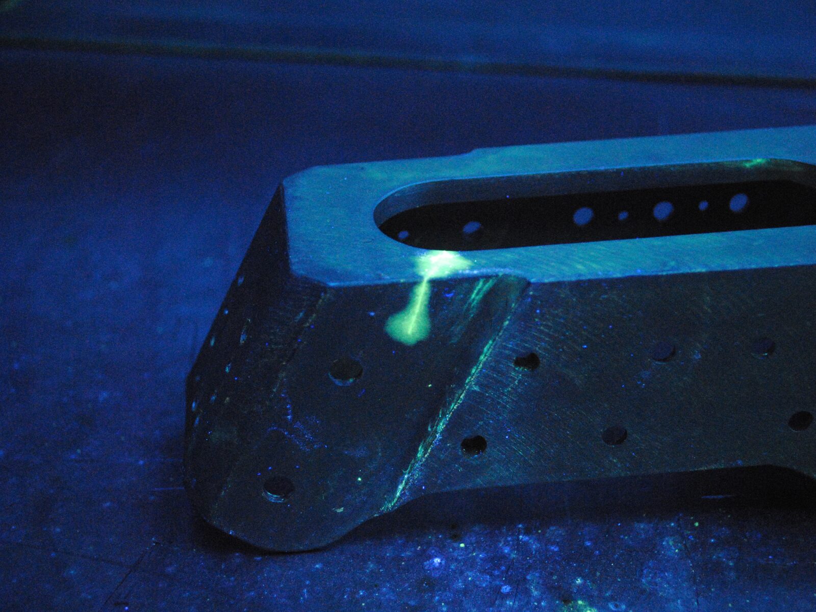 Welded metal component during liquid penetrant testing. Ultraviolet light illuminates the green dye that seeps through a corner crack.