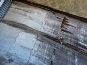 Large industrial dam. A rope access technician studies a leak on the concrete. He looks tiny by comparison.