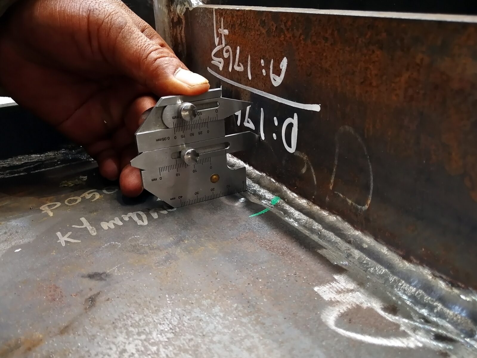 Weld inspector measures the dimensions of a fillet weld. White chalk identifies the parts and defects.