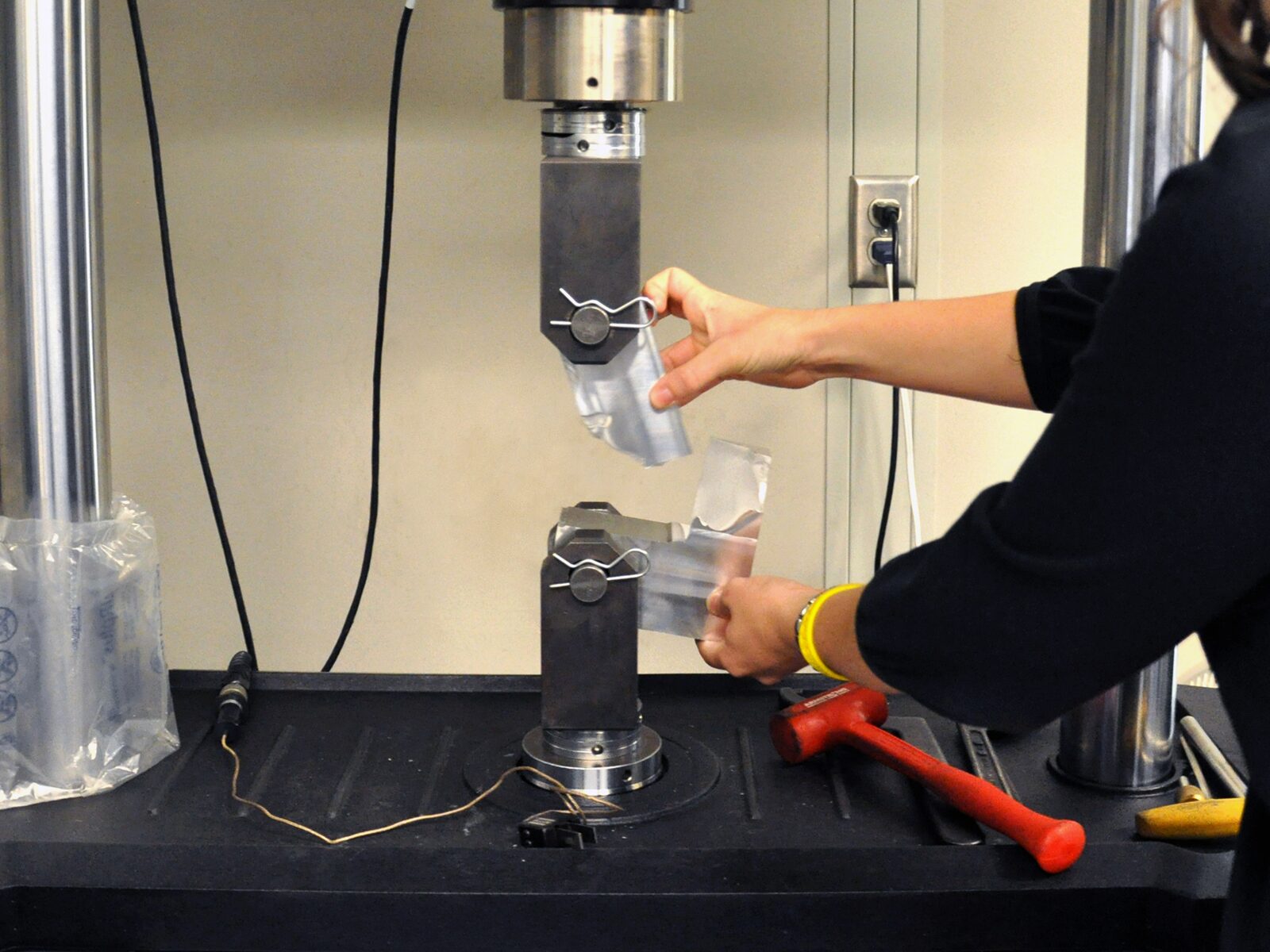 Lab technician holds two parts of a ruptured plastic sample after material fatigue testing.