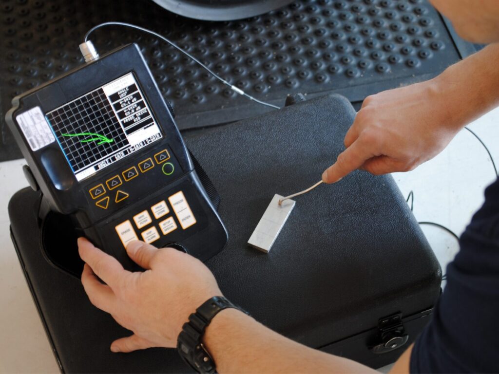 Over the shoulder photo of a technician using an Eddy Current tester at an airplane hangar