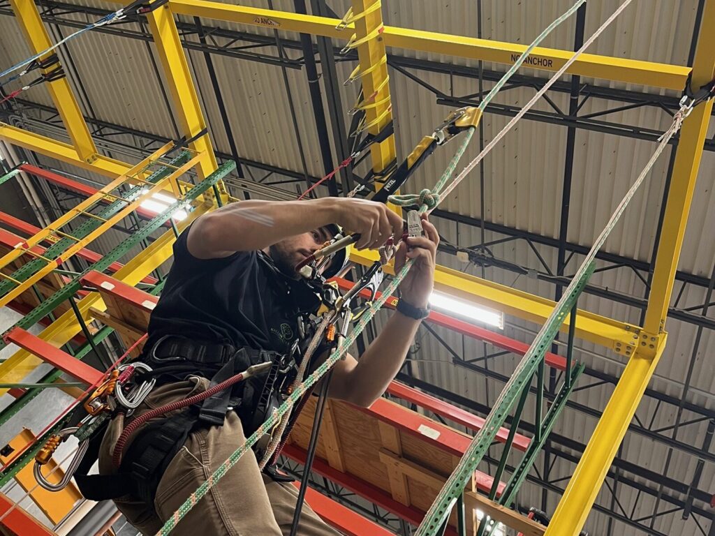 A suspended rope access technician adjusts his ascender on a rope training course.