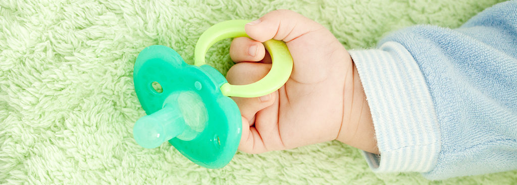 baby's hand holding a green pacifier