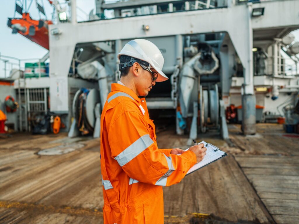 Inspector on a ship deck takes notes on a clipboard.