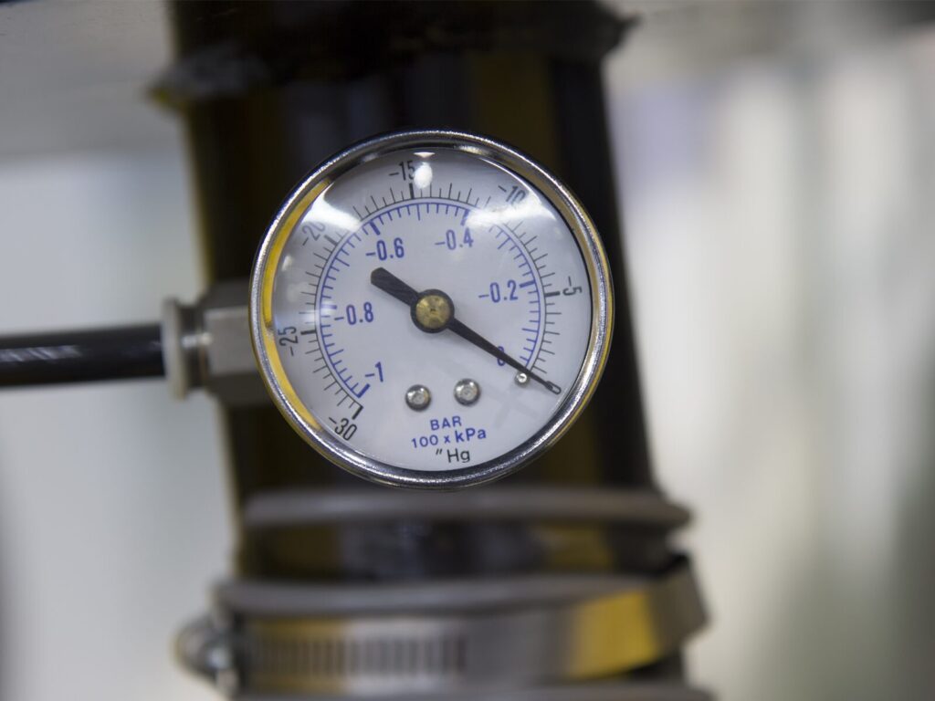 Focus on a dial vacuum gage with a pump in the background