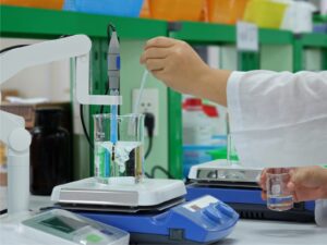 Chemist positions a solution on a hot plate. A pH meter is partially submerged in the solution.