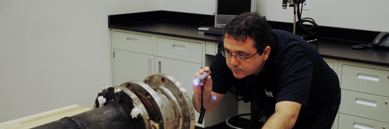 Engineer points a flashlight at a large pipe in a lab