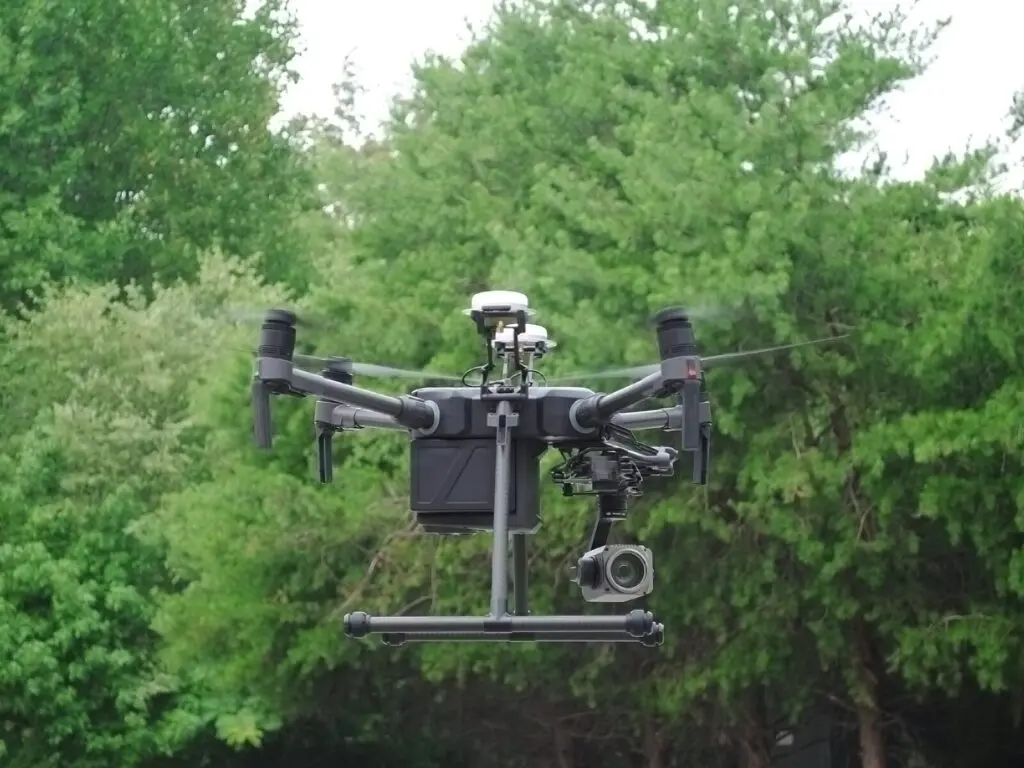 Unmanned aerial vehicle, or drone, hovers in front of trees