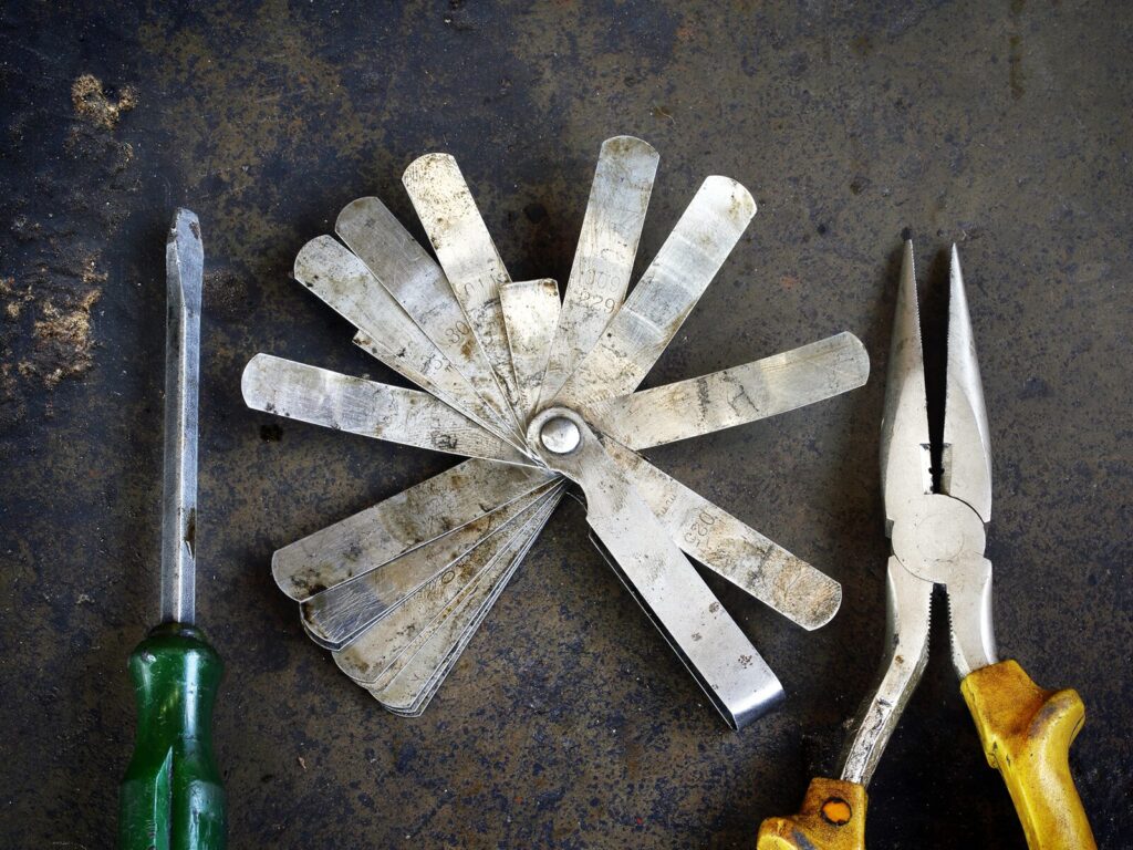 A screwdriver, a feeler gage, and a set of pliers