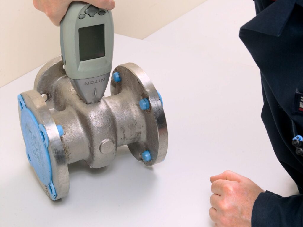 Chemist uses a handheld XRF machine for positive material identification (PMI) of alloys in a flow meter.