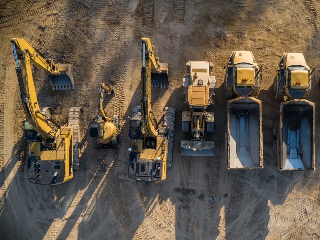 Construction equipment lined up at a site. Crane, trucks, and excavator.