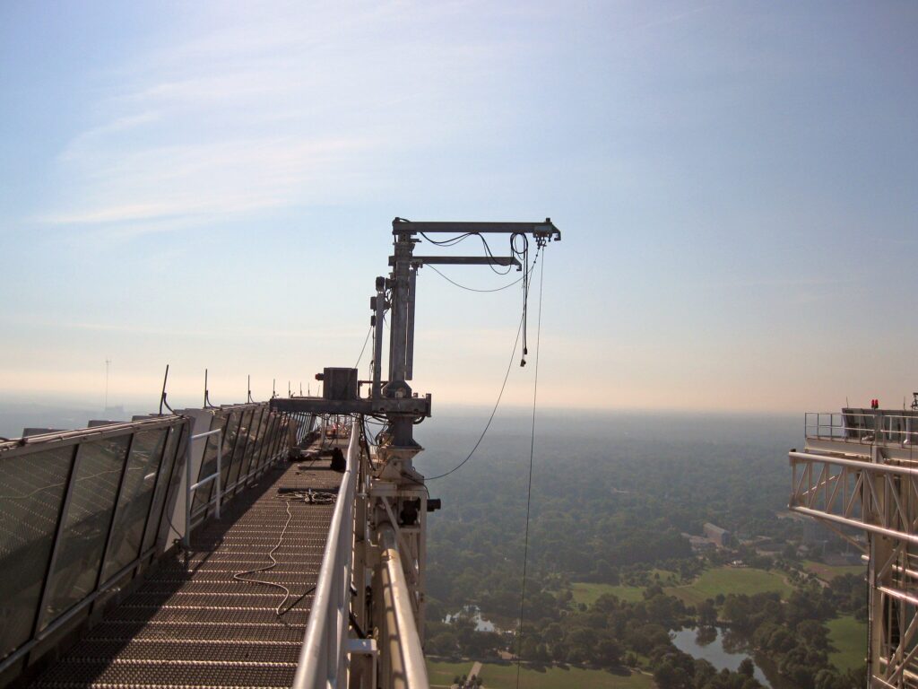 Roof davit system and guardrails along the edge of a multi-story building. In the distance is an expanse of forest and the horizon at dawn.