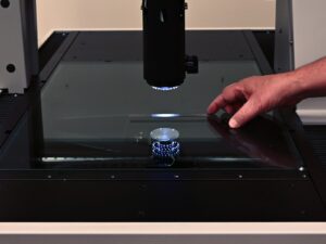 A lab technician places a ruler on a precision CMM machine surface