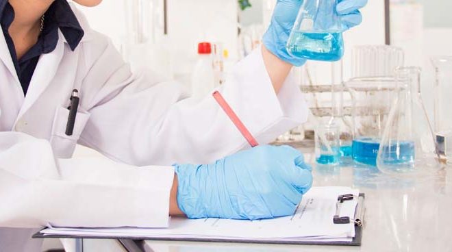 Chemist writing on clipboard while testing chemicals