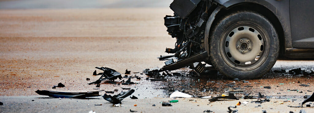 Debris from a front-end crash surrounds a black car. This debris is evidence for accident reconstruction engineering.
