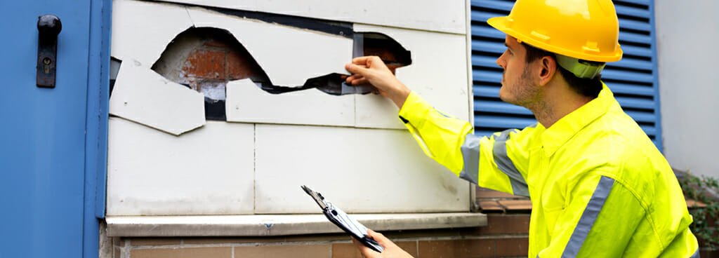 An inspector from a building inspection company examines the damaged cladding of a residence.
