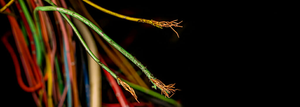 A tangle of frayed green, yellow, and red wires against a dark background during an electrical forensics investigation.