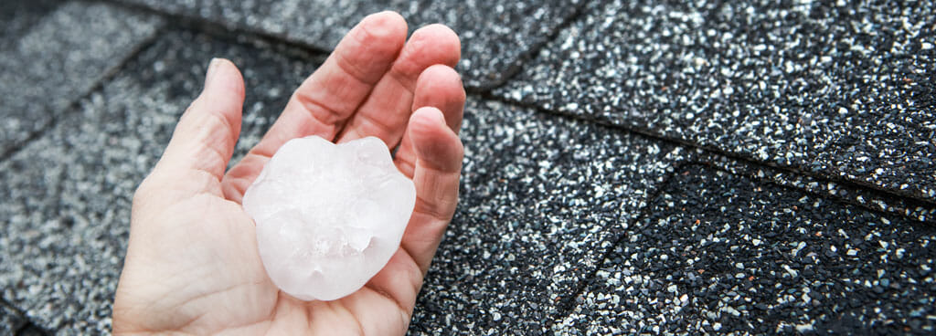 Hand Holding A Large Piece Of Hail While Inspecting A Roof