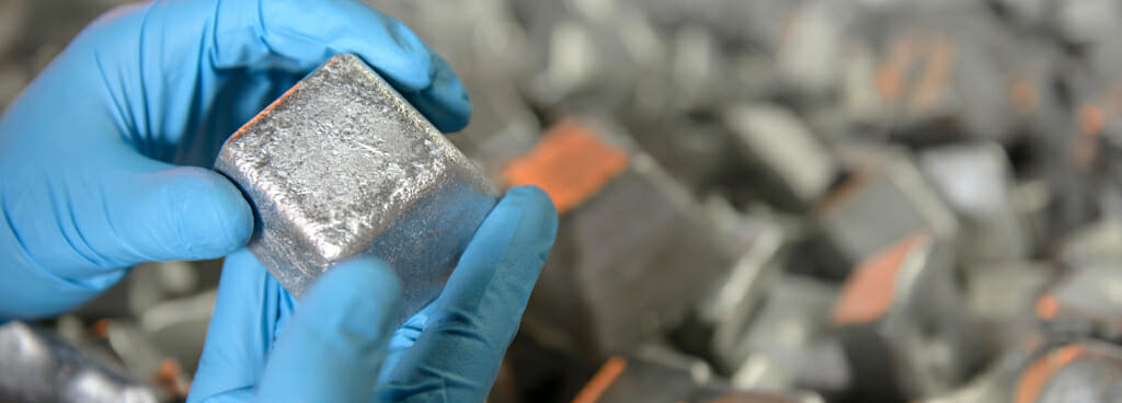 Metallurgist examines a scratched block of aluminum for forensic metallurgy. A pile of similar blocks is in the background.