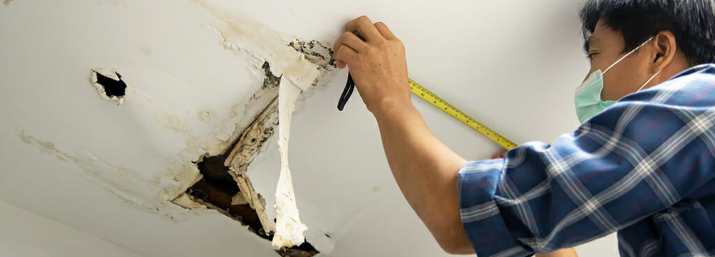 A man measures ceiling stains during a forensic water damage evaluation.