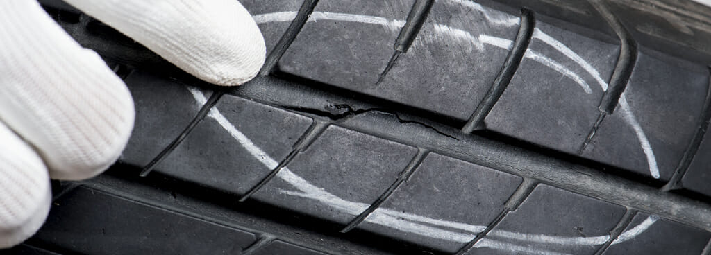 A tire failure expert points to a crack in the groove of a tire. The damage is circled with white chalk for easy identification.