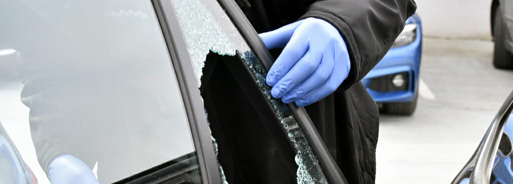 An investigator holds open a car door with a smashed window for vehicle forensics.