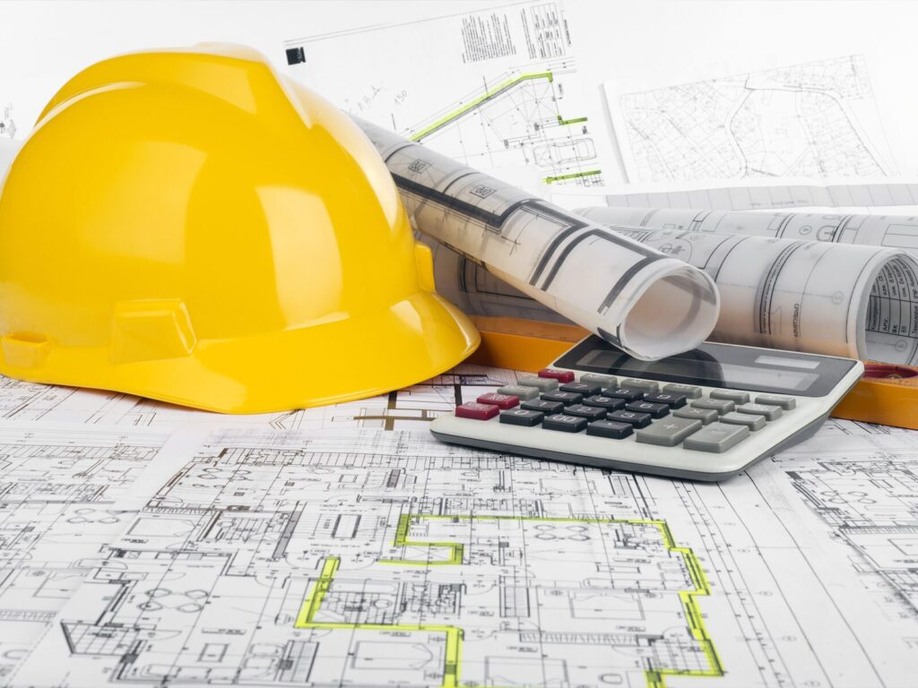 Yellow hard hat and calculator on top of building schematics and documents