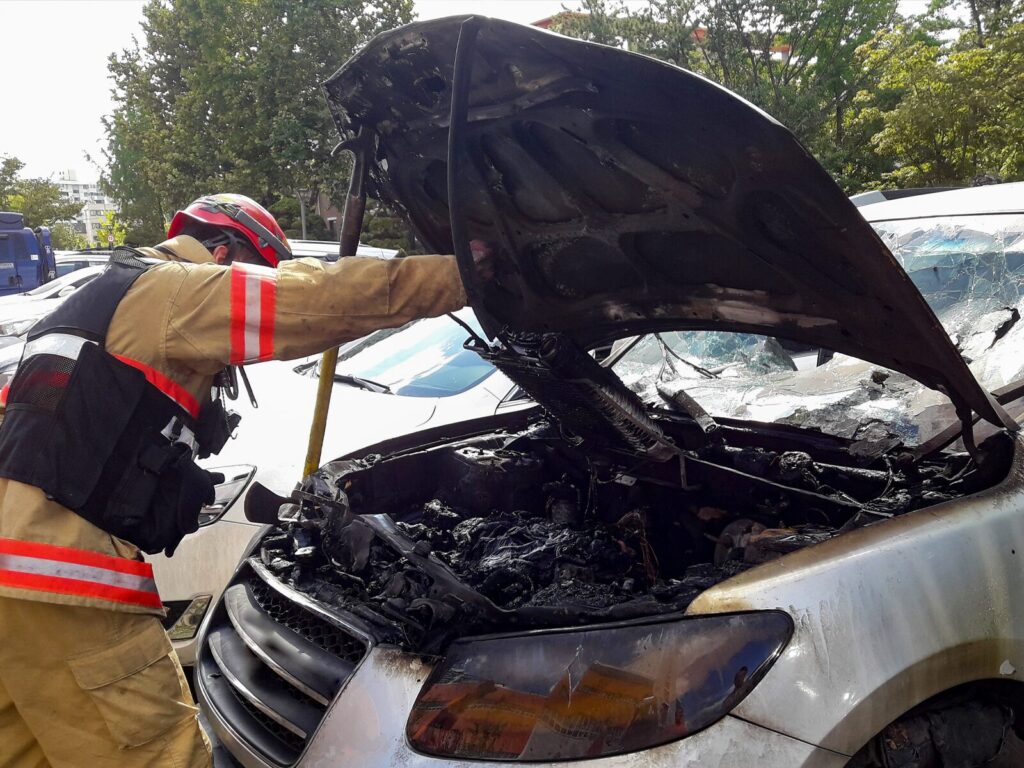 A firefighter pulls up the hood of a charred vehicle after an engine fire