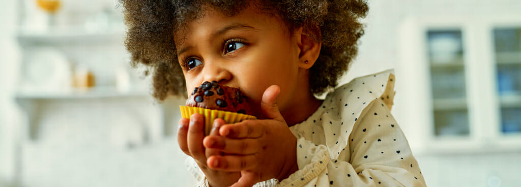 A very young girl savors a fresh chocolate cupcake, but there could be PFAS chemicals in the liner.