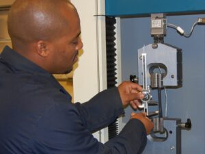 Technician measures a coupon's height change after tensile testing