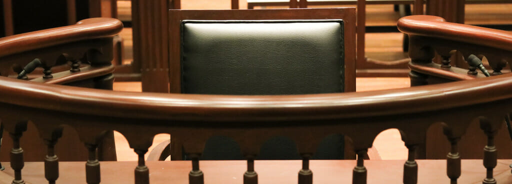 Witness stand in a courtroom. The chair is furnished with leather and dark wood. The bench is made of similar material.