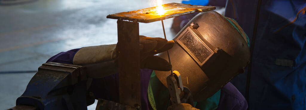 Welder uses the Shielded Metal Arc method for 4G welding certification. The welder aims the electrode overhead to fuse two plates.