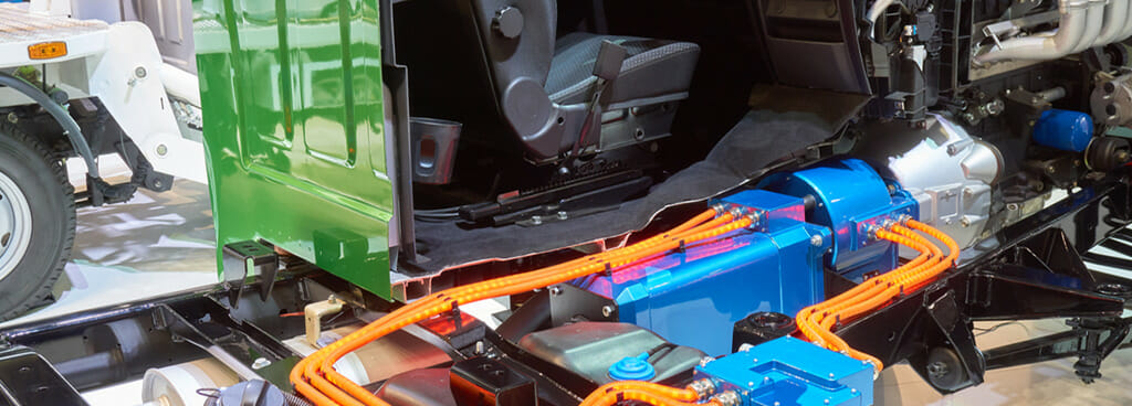 A cutaway of the tractor unit of an electric truck. The driver's seat and wheel are exposed, along with the electric battery beneath.