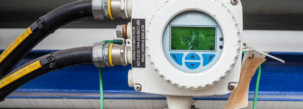A magnetic flow meter with digital display in a power plant. Two yellow cords connect the meter to the pipeline.