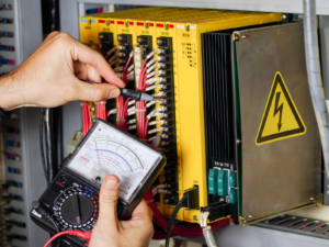 Electrician uses an analog multimeter to test a circuit board in an industrial plant.