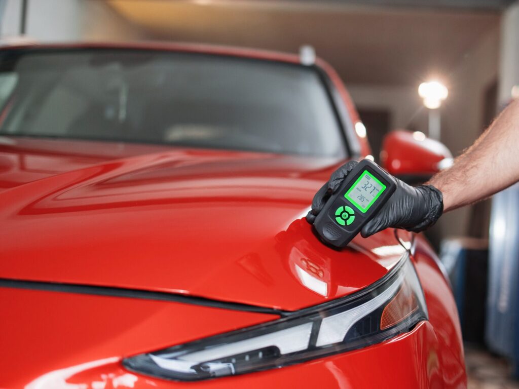 Technician uses a positector to measure the coat of red paint on the hood of a car