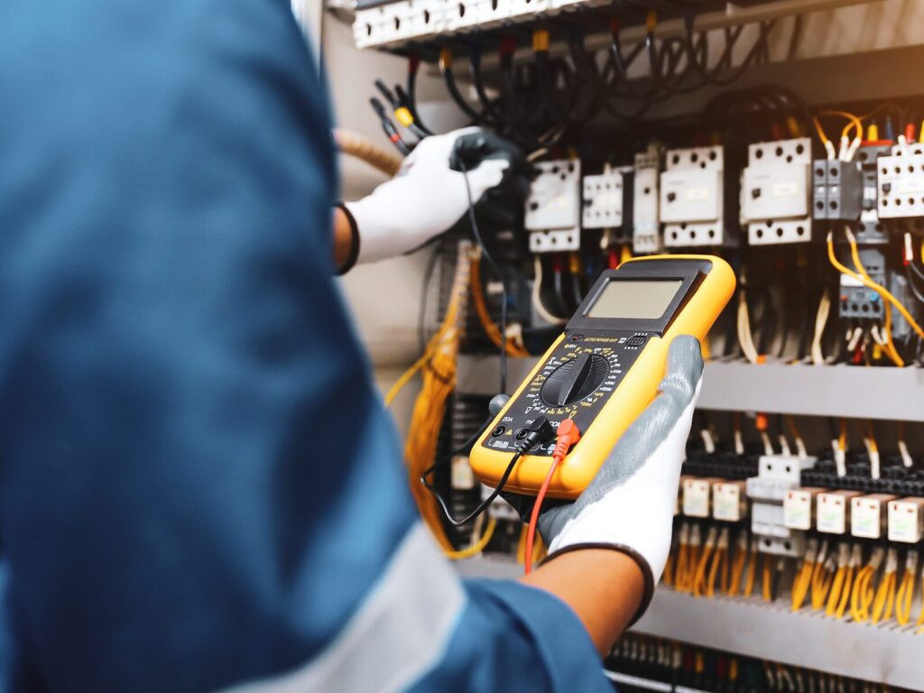 Electrician uses a digital multimeter to measure flow in an electrical cabinet